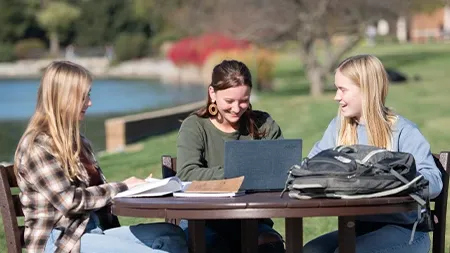 Three female college students studying at table outside