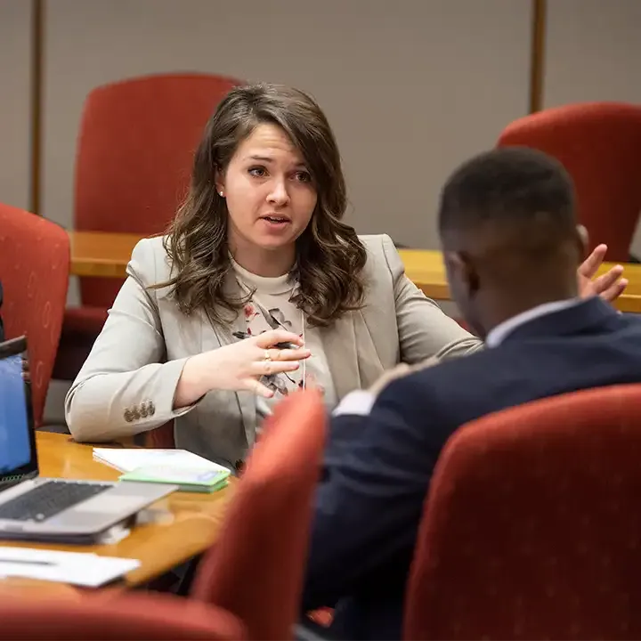 Man and woman in business attire sitting and talking at a conference table.